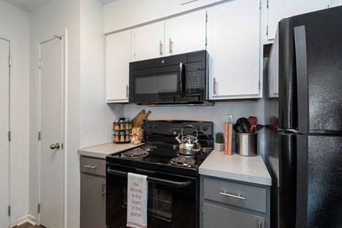 A kitchen with a black appliances and an electric range, featuring gray and white cupboards.