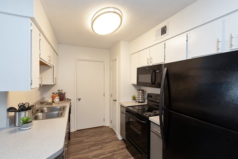 A kitchen with black appliances and white cabinets is featured, along with white specked countertops.