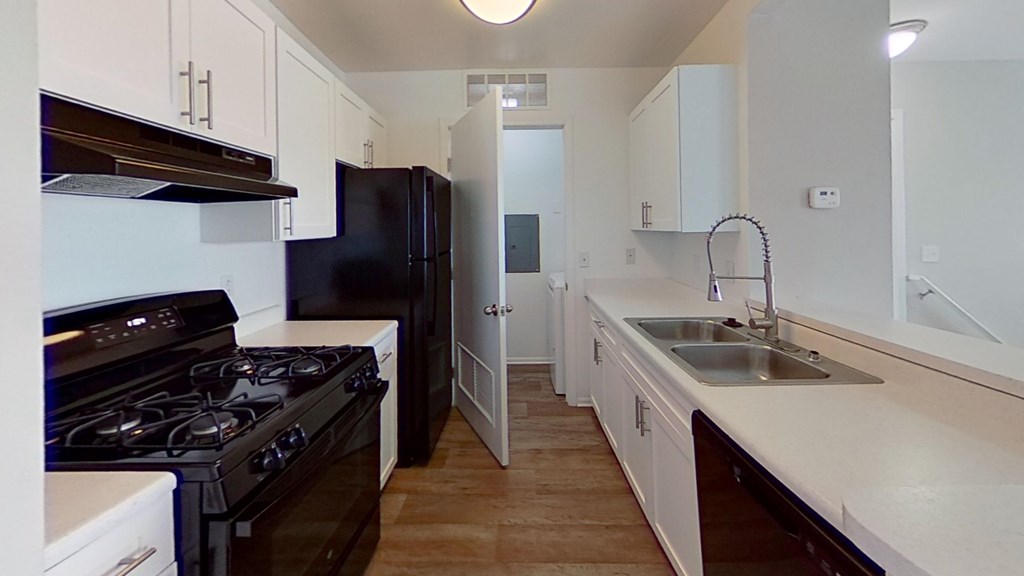 A kitchen with black appliances and white countertops and wood-style floors.