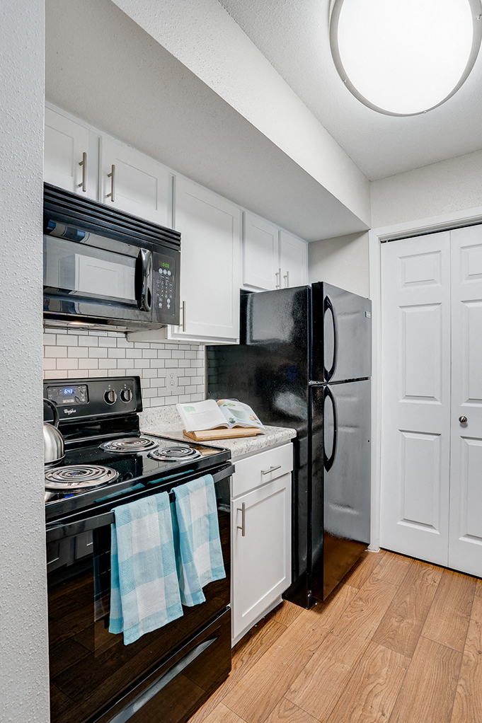 A black refrigerator is in a kitchen with white cabinets and a black stove.