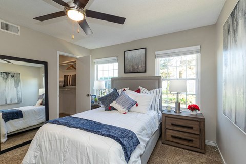 A spacious bedroom with a large bed, a ceiling fan, and two windows.