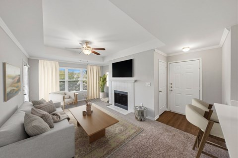 A living room with a grey couch, a coffee table, a flat screen TV, a fireplace, and a ceiling fan.
