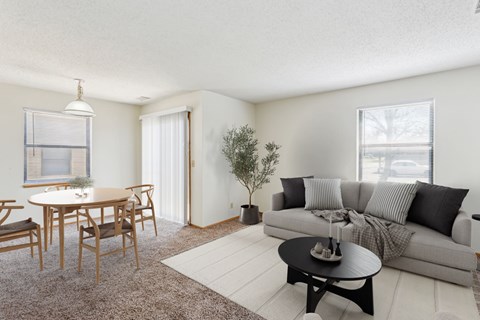 A living room with a grey couch, a wooden dining table with chairs, and a small tree.