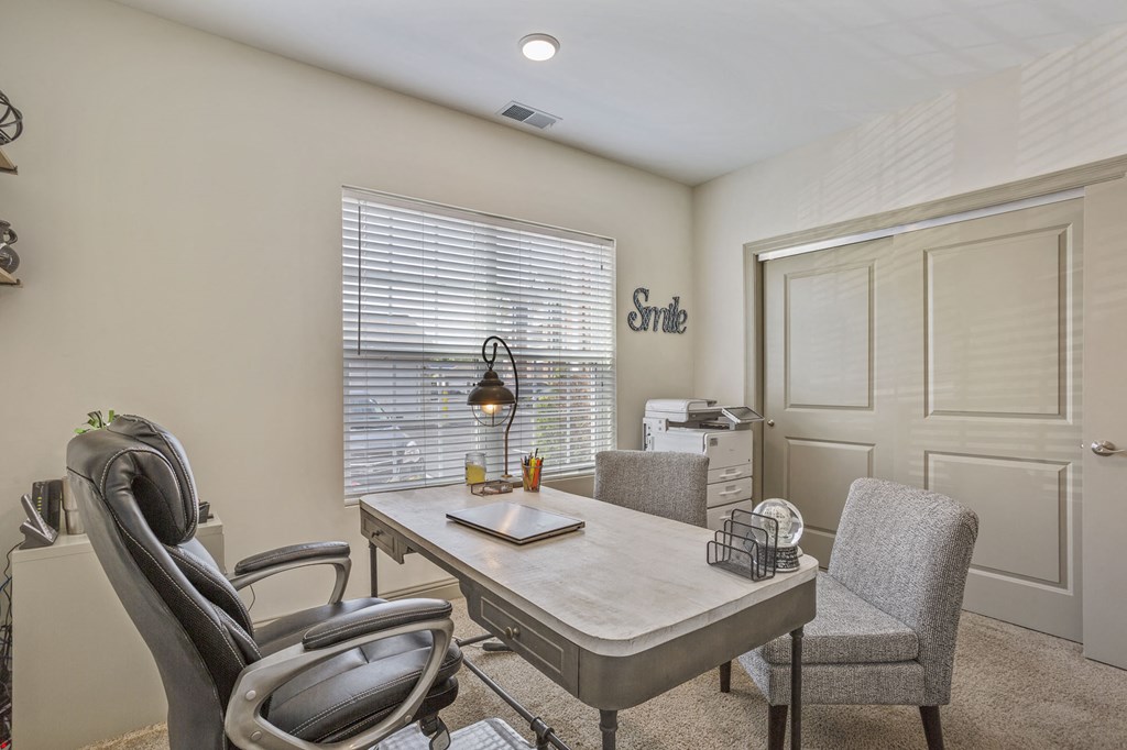 a home office with a desk and chairs and a window