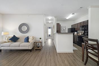 a living room with a couch a table and a chair and a kitchen with a stove and