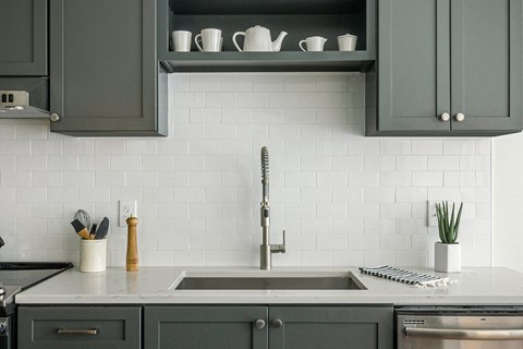 a kitchen with gray cabinets and white tiles and a sink