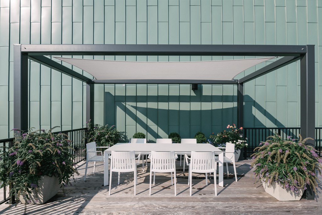 Dining table under awning on Rooftop lounge, surrounded by large potted plants