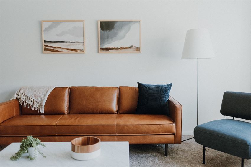 a living room with a brown couch and two paintings on the wall