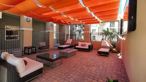 Redlands, CA, Pet-Friendly Apartments - Circa 2020 - Community Room with Patio Flooring Made of Patterned Pavers with an Overhead Canopy, Sofas, Chaise Lounges, Fire pit, and Mounted Televisions.