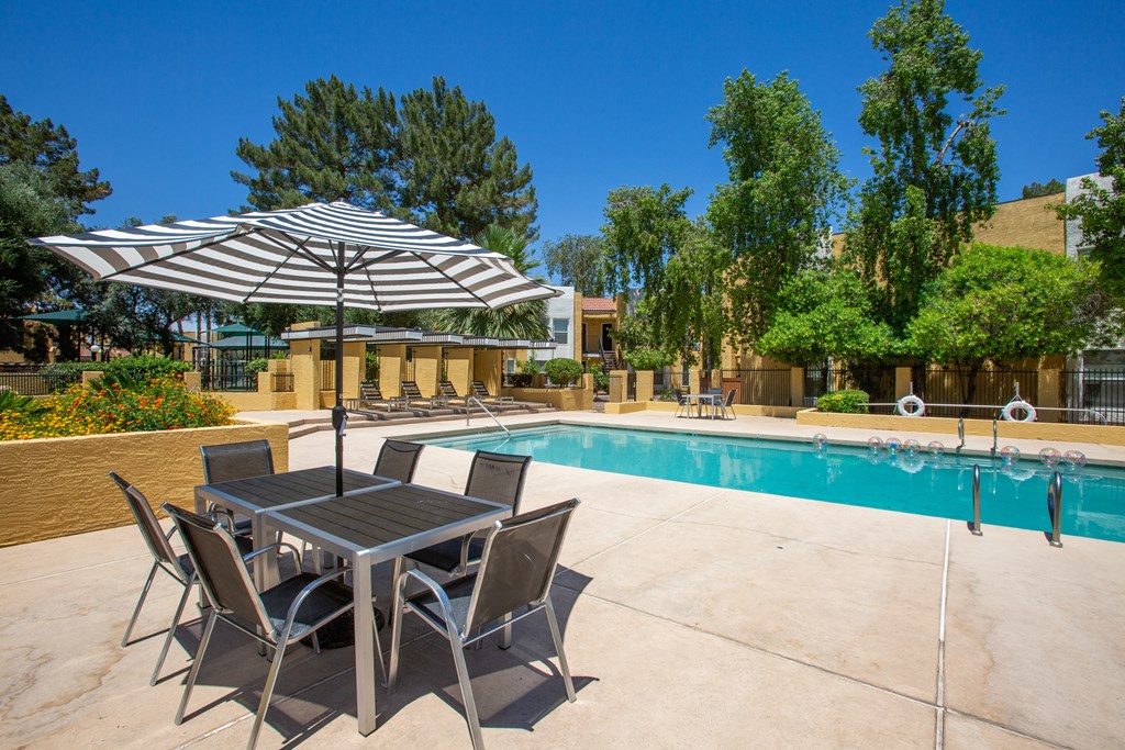 a swimming pool with a table and chairs under an umbrella at Ascent on Peoria Apartments, Arizona