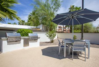 a patio with two bbq grills and a table with chairs and an umbrella at 60 at Melrose in 85013 Phoenix, AZ