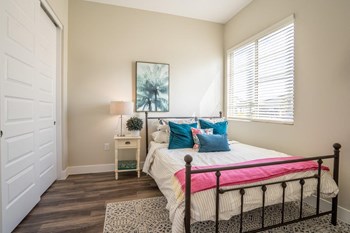 A large bed with a nightstand sits in a bedroom with double closet doors and a window at Village Greens of Queen Creek - Photo Gallery 5