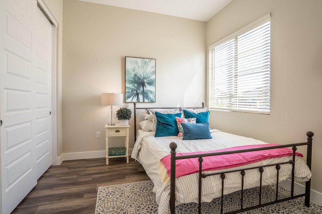 A large bed with a nightstand sits in a bedroom with double closet doors and a window at Village Greens of Queen Creek