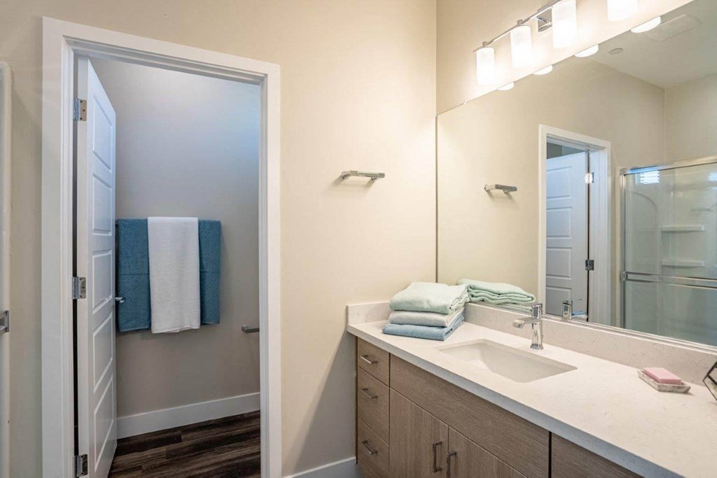 Model bathroom has a long mirrored vanity sink with storage in an apartment at Village Greens of Queen Creek