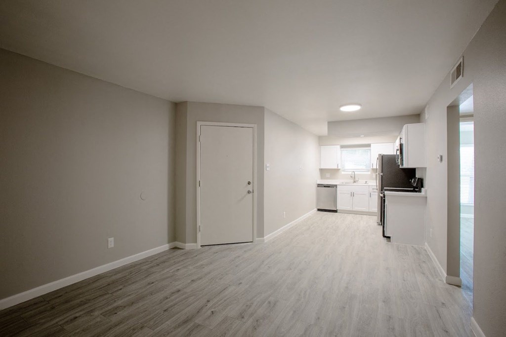 an empty room with a kitchen in the background