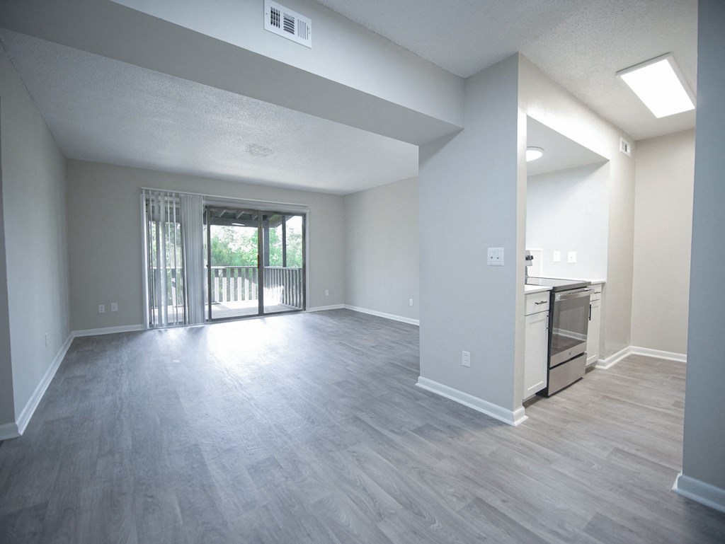 an empty living room and kitchen with a sliding glass door to a balcony