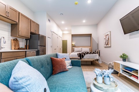 A living room with a blue couch and a kitchen area with wooden cabinets.