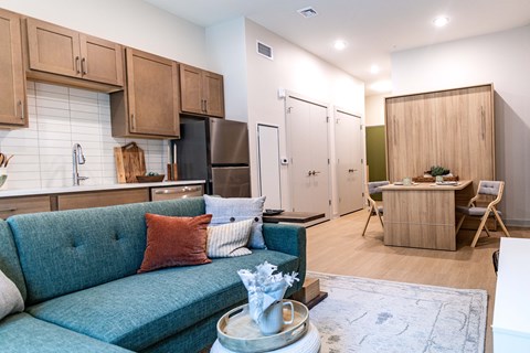 A blue couch with a red pillow is in the middle of a kitchen and living room.