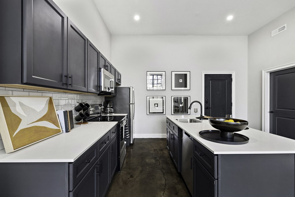 an open kitchen with black cabinets and white countertops and a large sink and counters