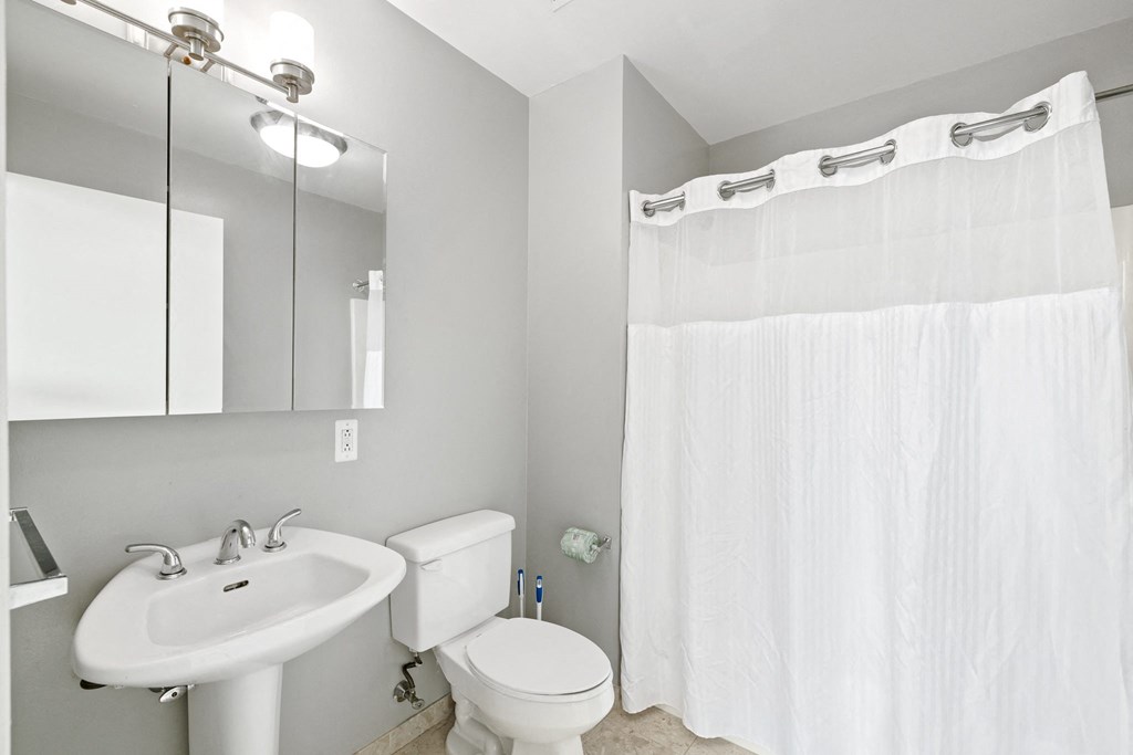 a bathroom with a white sink and toilet next to a white shower curtain