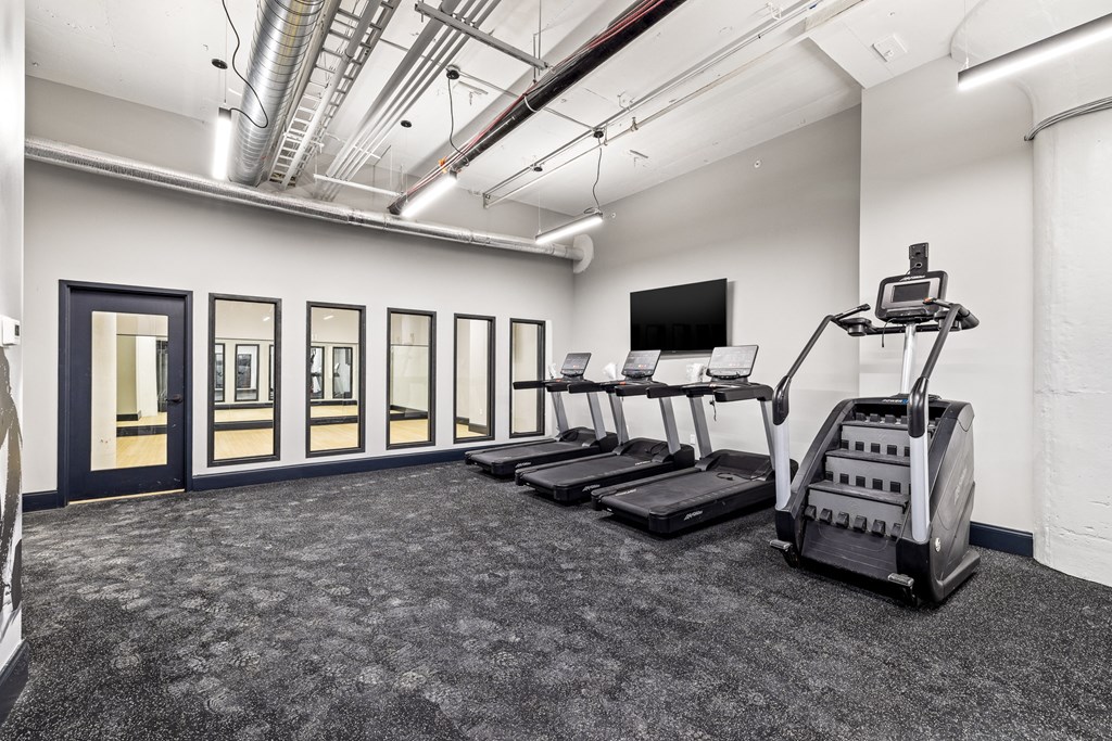 a gym with treadmills and weights in a room with windows