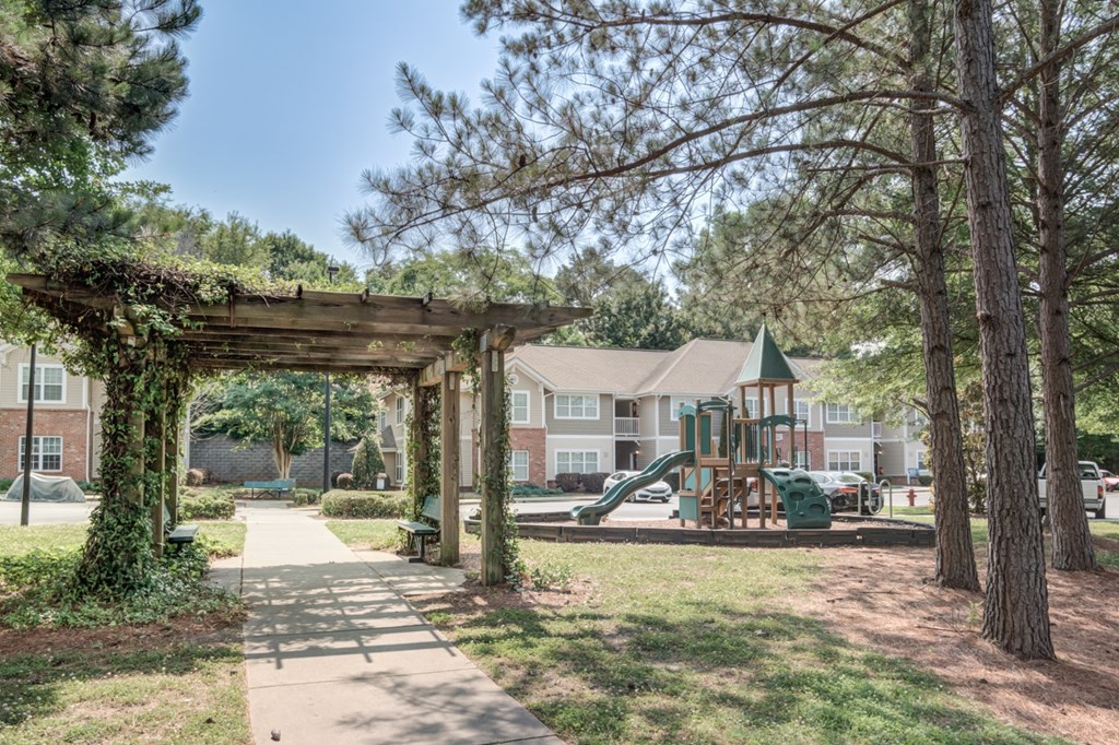 A playground with a green slide and a wooden pergola.