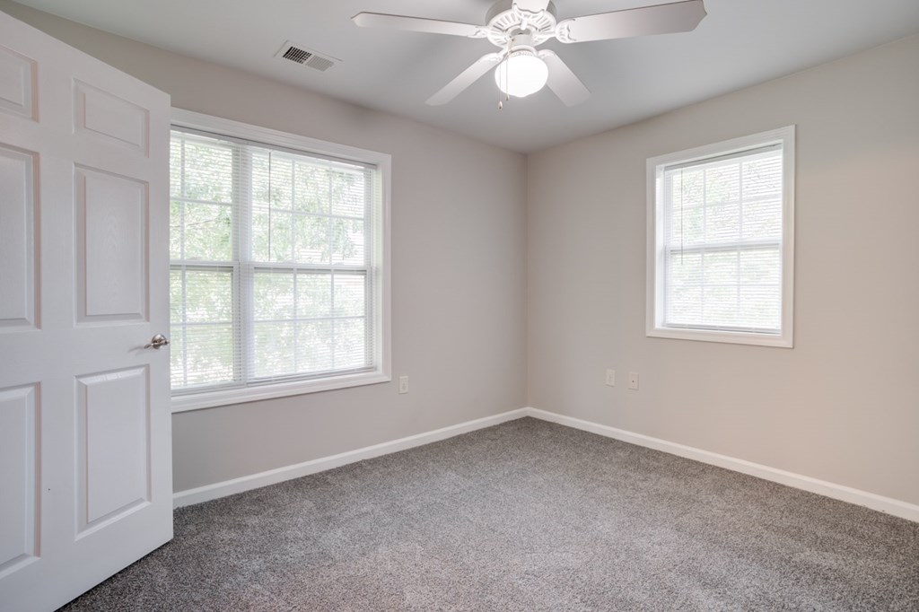 A room with a ceiling fan and two windows.