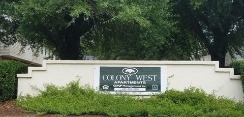 a sign for colony west apartments in front of a tree