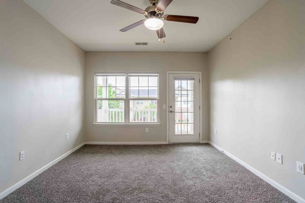 Bright living room with ceiling fan, plush carpet flooring, and direct access to private balcony at Cedar Terrace Apartments Hendersonville, NC 28792