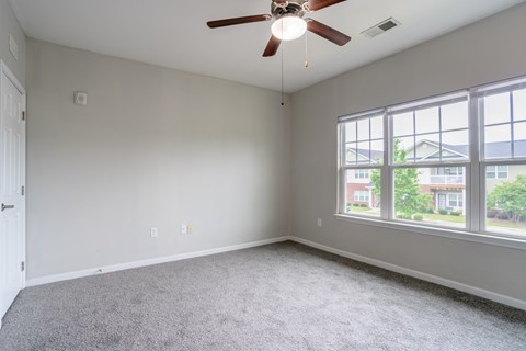 Large bedroom with neutral tones, carpet flooring, ceiling fan, and oversized windows offering abundant natural light at Cedar Terrace Apartments in Hendersonville, NC 28792