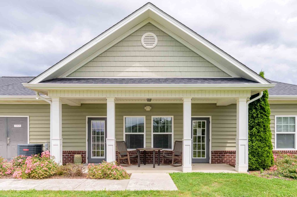 Inviting clubhouse exterior with covered front porch, patio seating, and manicured landscaping at Cedar Terrace Apartments in Hendersonville