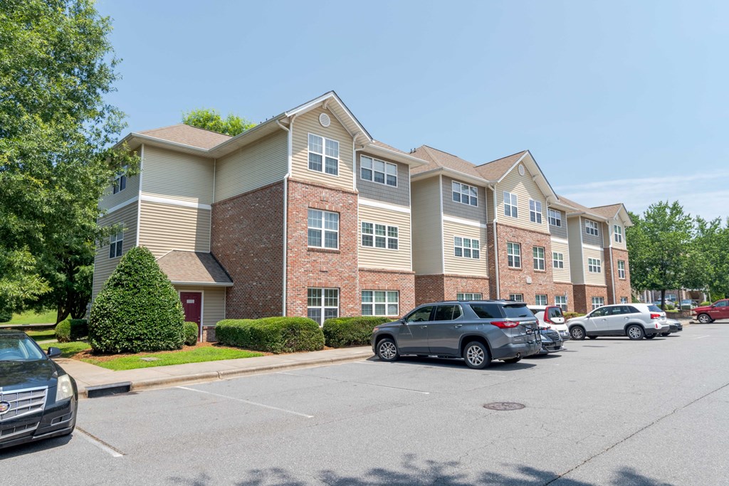 A parking lot in front of a multi-story apartment building with cars parked.
