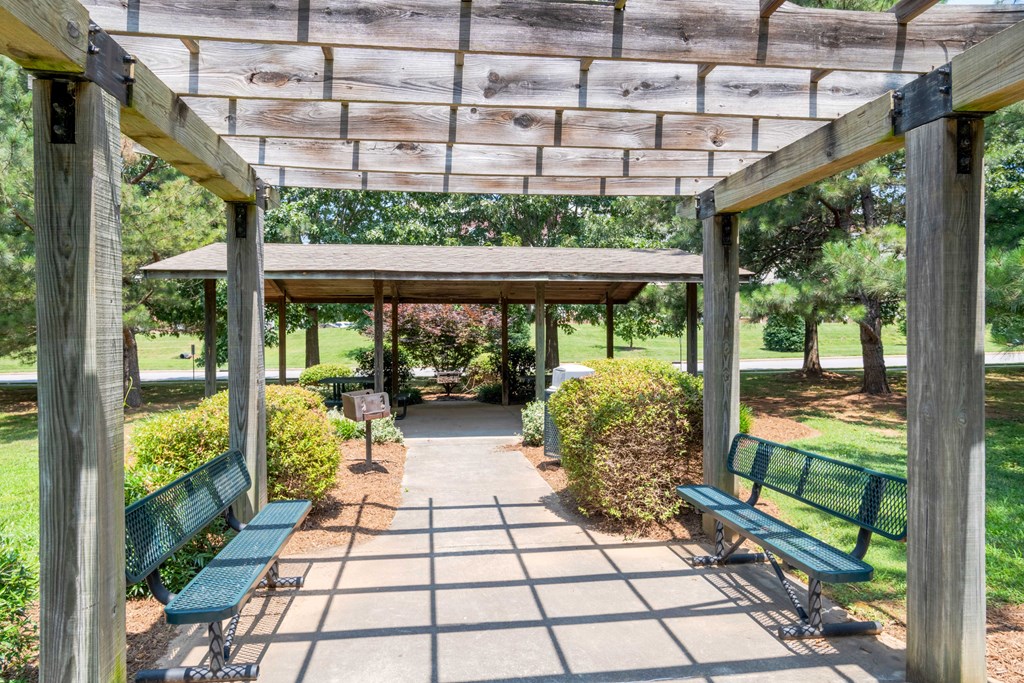 A wooden pergola with green benches is in a park.
