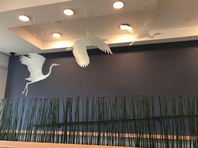 a wall with two cranes flying over a field of bamboo