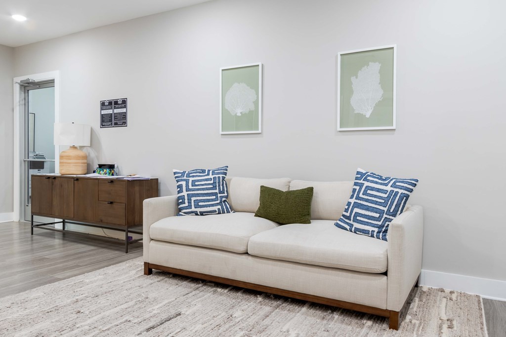A white couch with blue and green pillows sits in a room with a wooden floor and two framed pictures on the wall at James Lewis Jr, Charleston