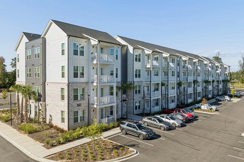 A row of white apartment buildings with cars parked in front.
