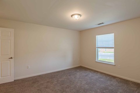 A room with a carpeted floor, a window, and a door.