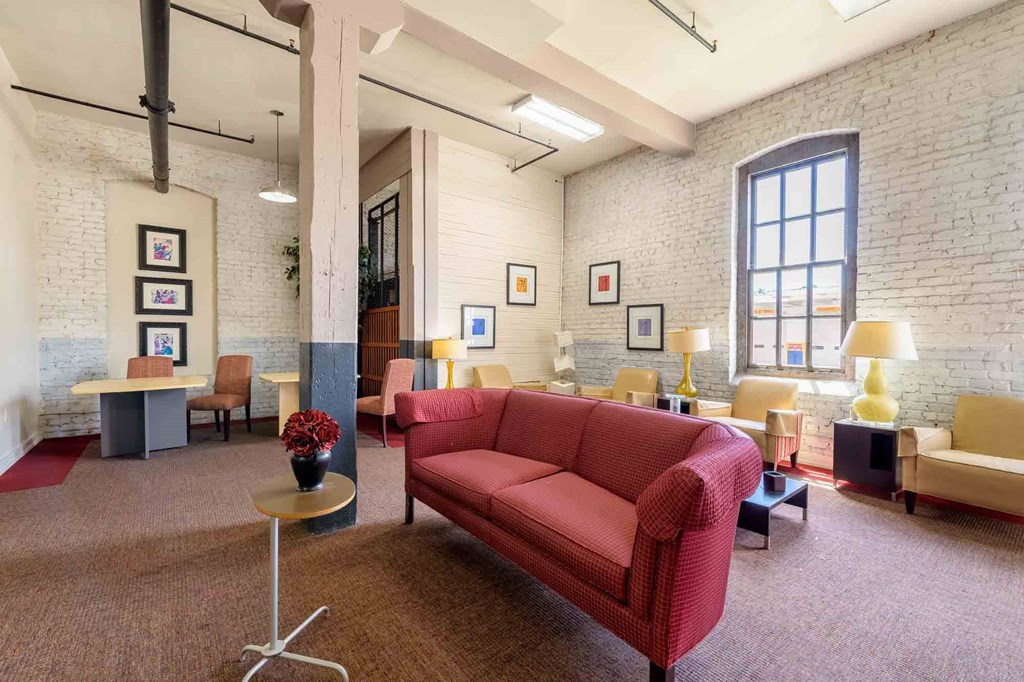 A red couch is in the middle of a room with a carpet at Nantucket Lofts Apartments, Kinston, North Carolina