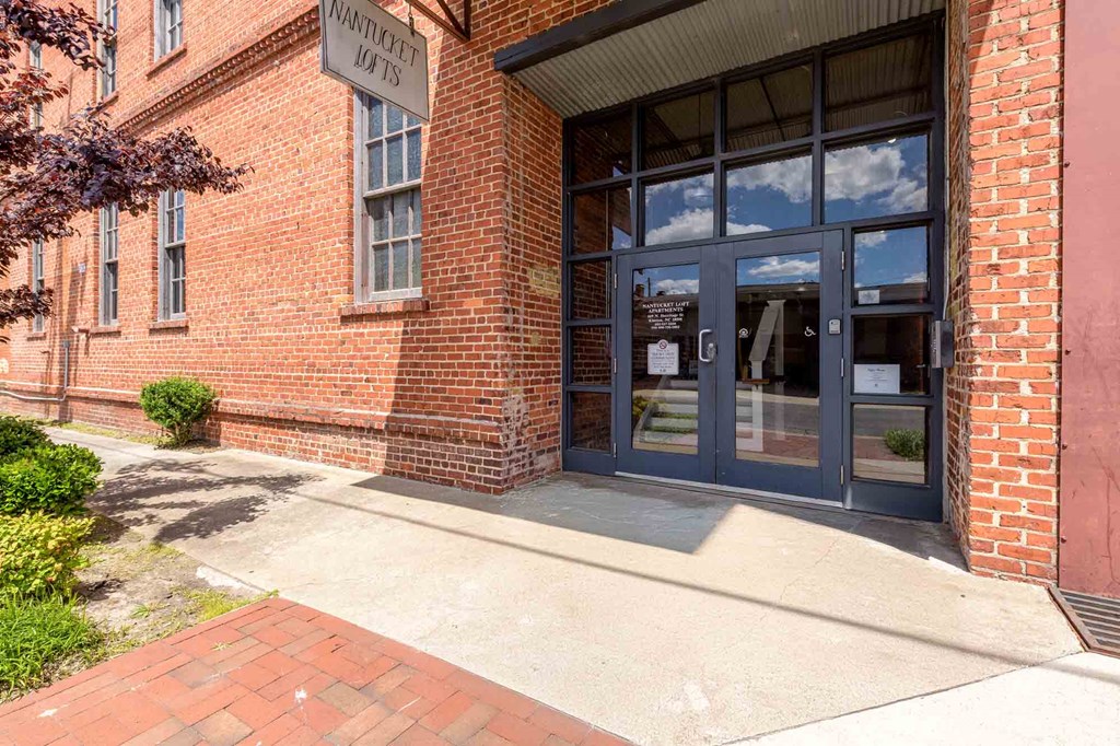 The front of a brick building with a glass door and windows at Nantucket Lofts Apartments, North Carolina, 28501