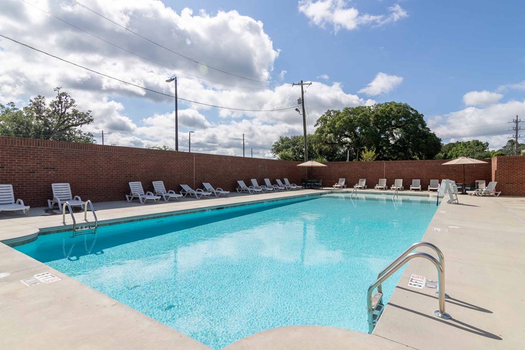 A large outdoor swimming pool with sun loungers and a brick wall.