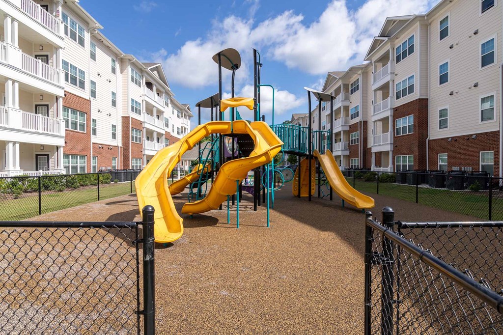 A playground with a yellow slide in front of apartment buildings.