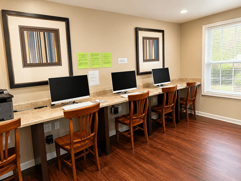 A room with a desk and chairs and two computers.