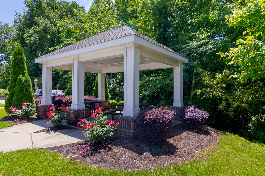 Covered Outdoor Pavilion with Picnic Tables Landscaped outdoor pavilion with brick accents, picnic seating, and flower beds, offering shaded relaxation at Snowden Senior Apartments.