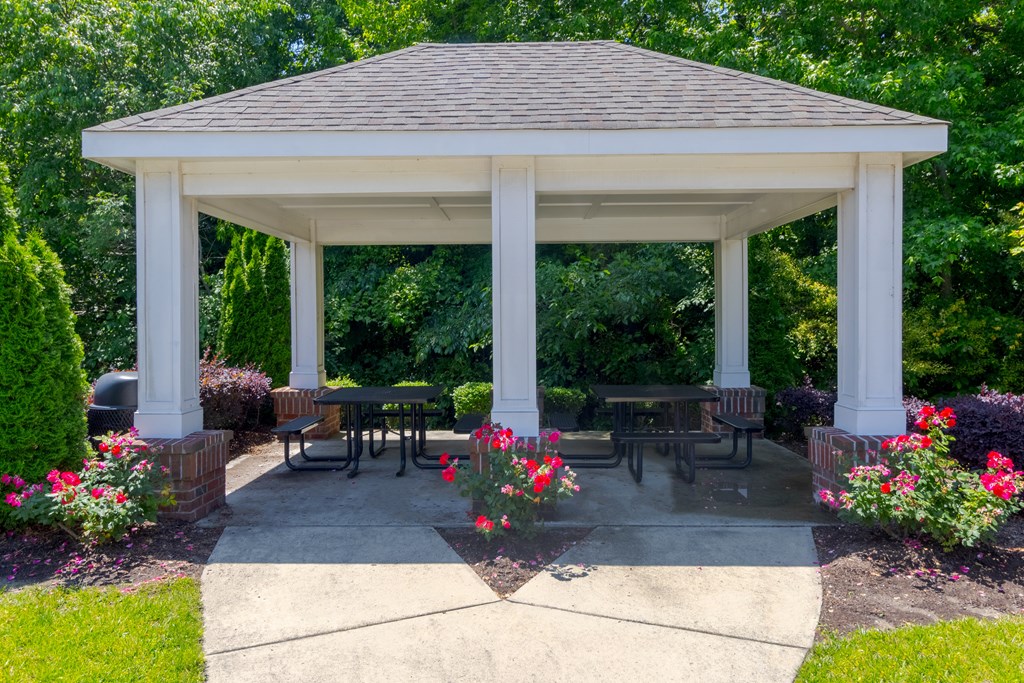 Covered outdoor pavilion with picnic tables, blooming flower beds, and lush green backdrop, ideal for socializing at Snowden Senior Apartments.