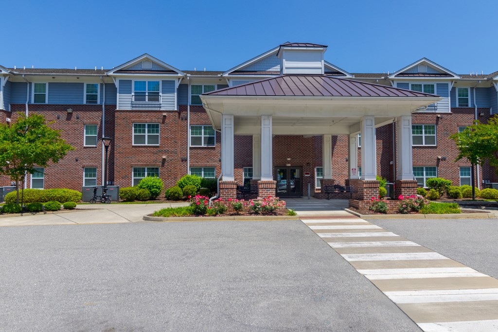 Main Entrance with Covered Drop-Off Area Front entrance of Snowden Senior Apartments featuring a large covered portico, landscaped walkway, and accessible crosswalk for residents and guests.