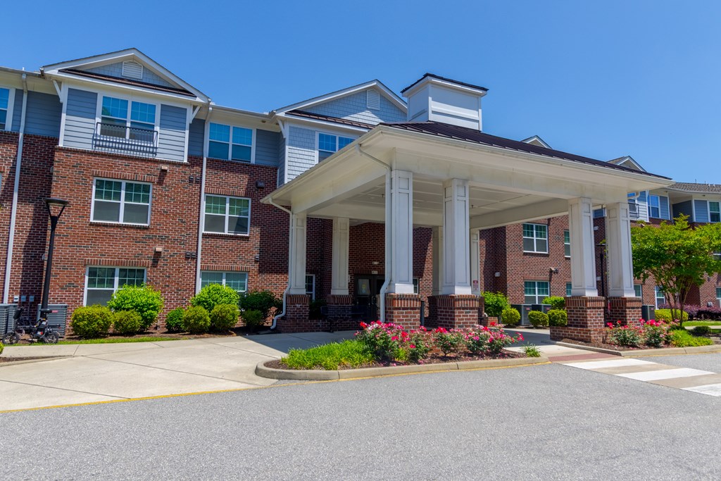 Elegant Front Entry and Landscaping Beautifully maintained front entry with brick facade, manicured shrubs, and architectural portico at Snowden Senior Apartments.