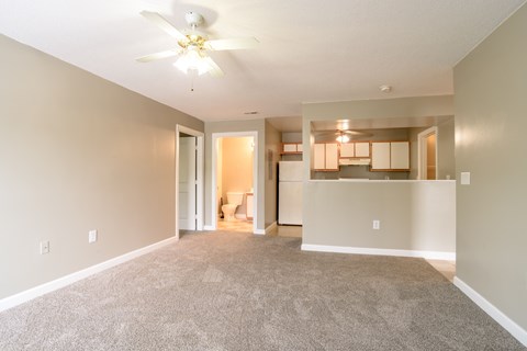 A living room with a carpeted floor and a ceiling fan.