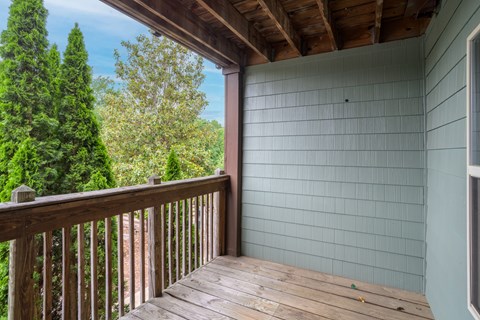 A wooden deck with a railing and a view of trees.