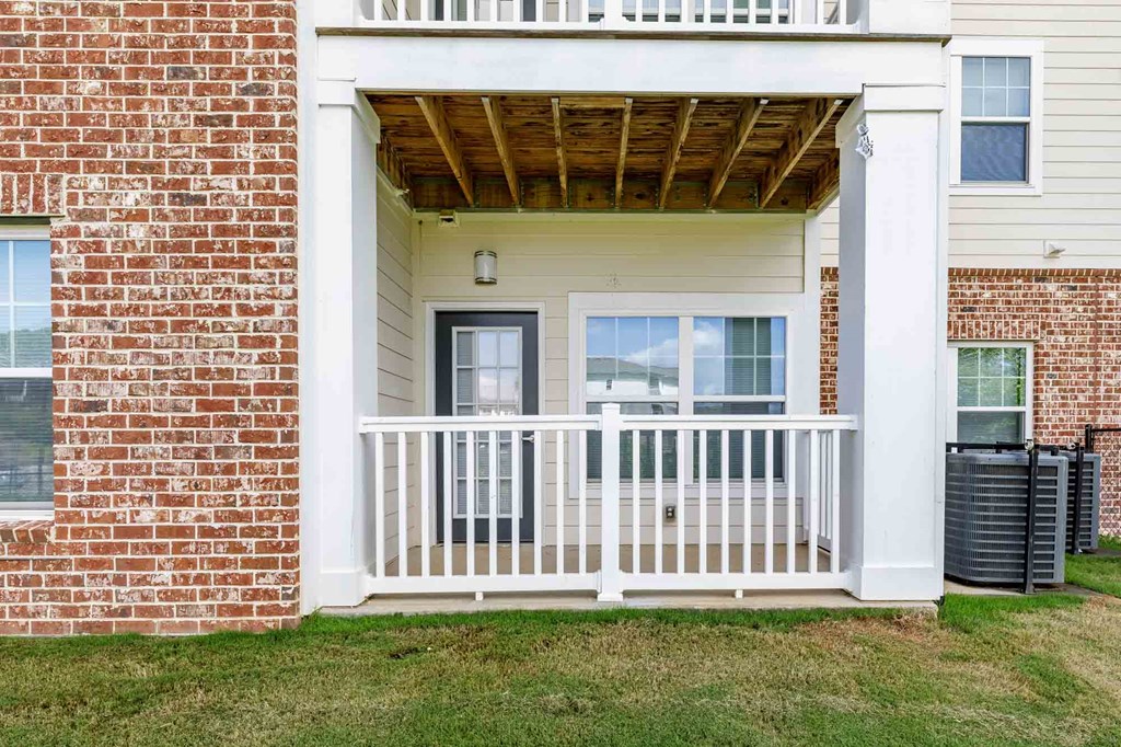 A white porch with a black trash can on the grass.
