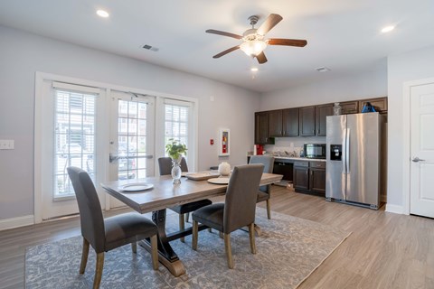 A dining room with a table and chairs and a kitchen in the background.